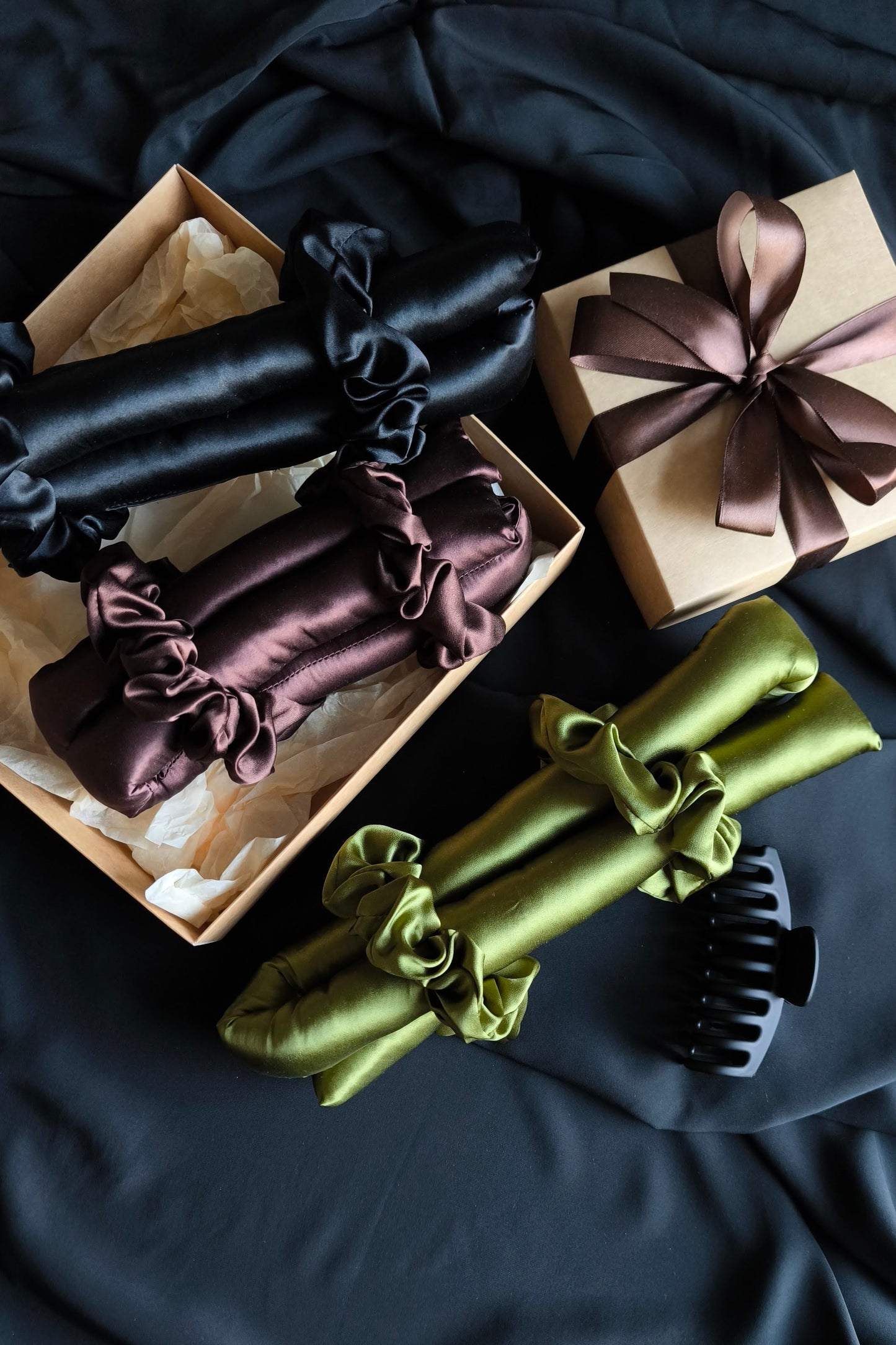 Set of hair scrunchies and hair curlers in various colors with packaging on a dark fabric background