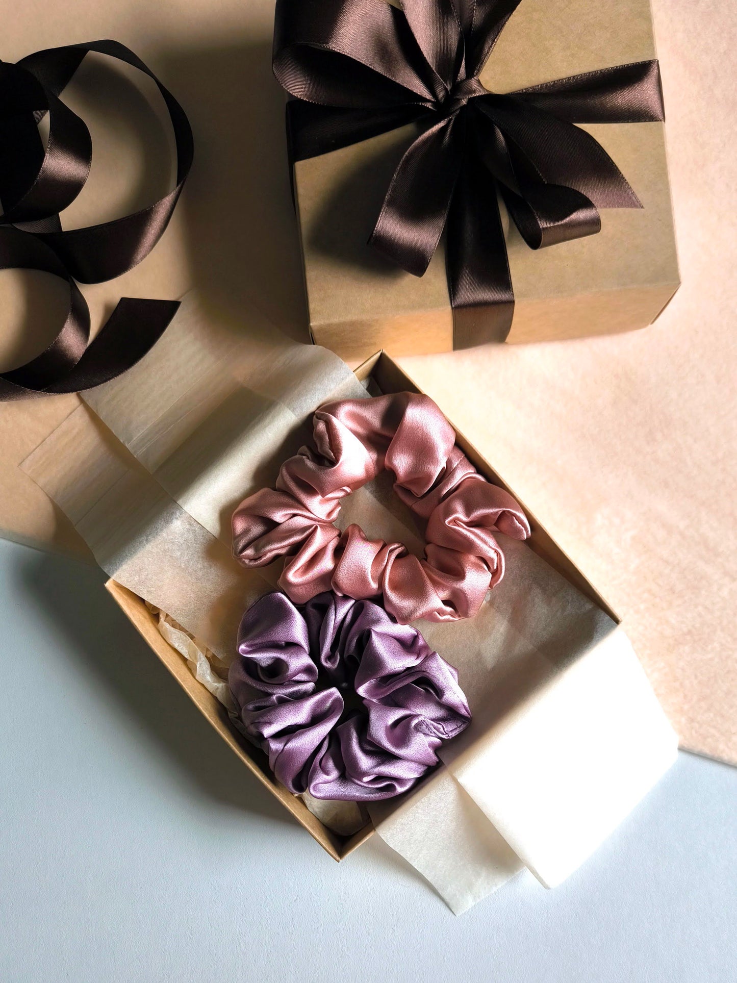 Two satin scrunchies in a gift box with ribbons on a light background