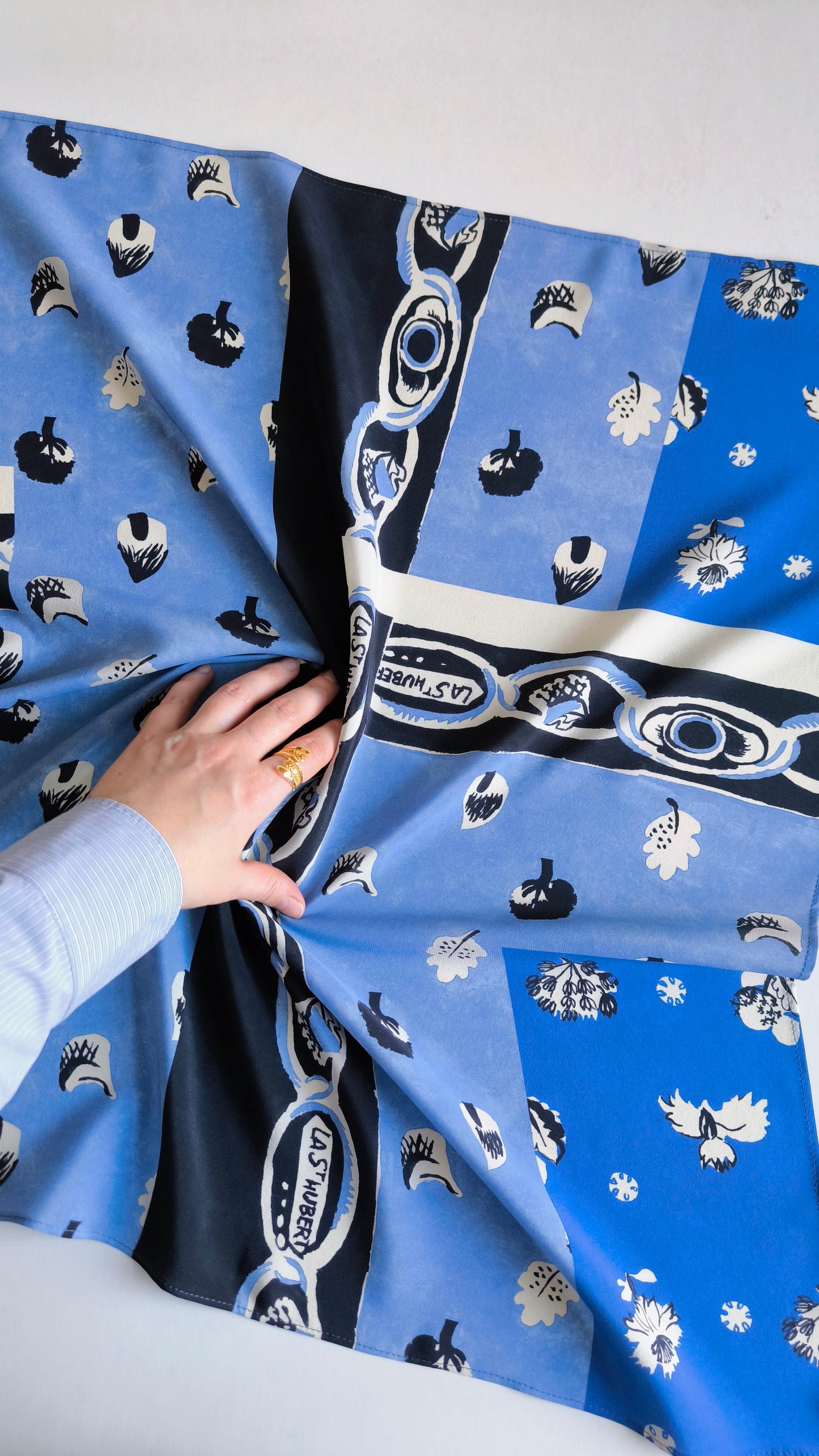 Blue fabric with black and white patterns, held by a hand against a light gray background