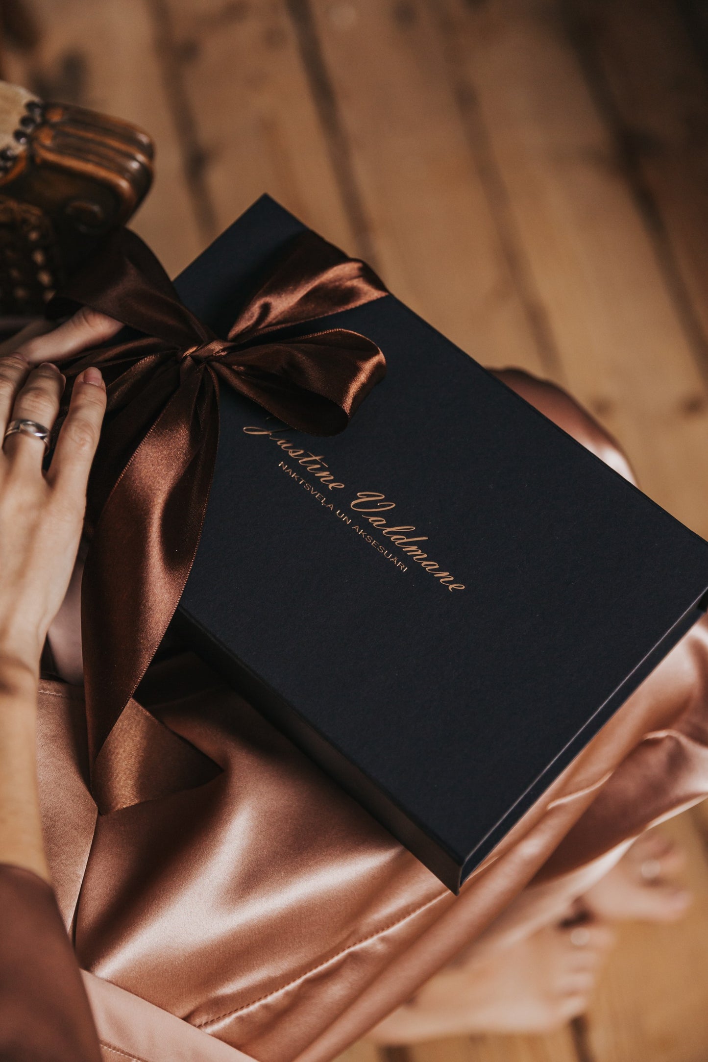 Black gift box with a brown ribbon held by hands on a wooden surface