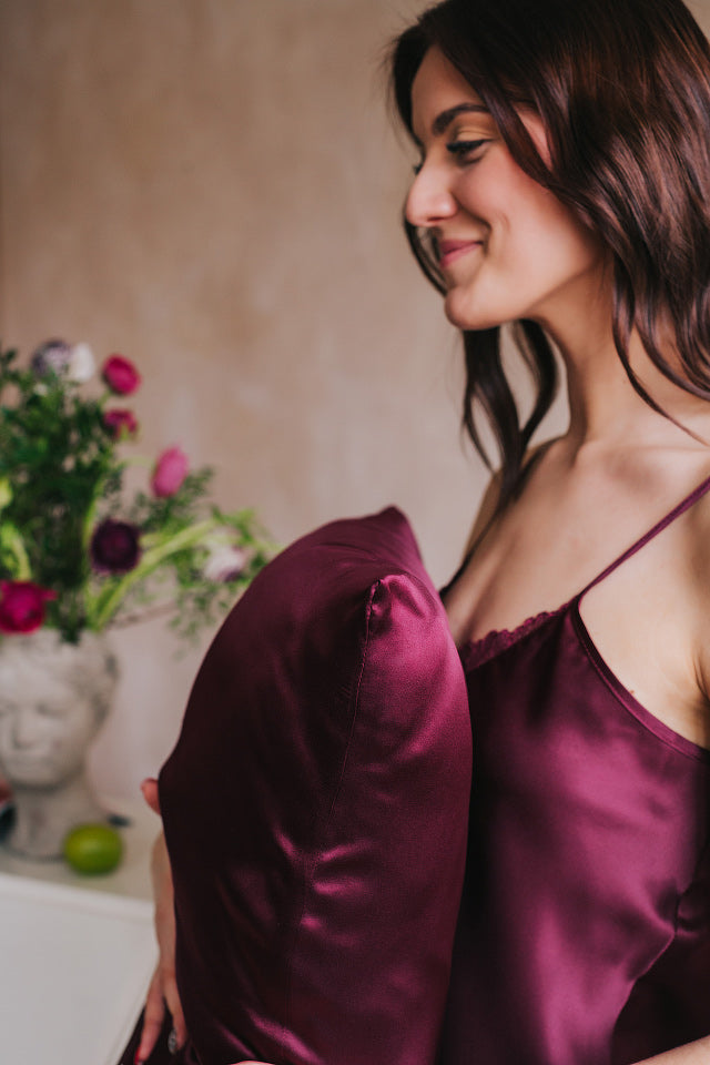 spilvens ar bordo krāsas dabīgā zīda spilvendrānu, sievietei rokās, profila bilde