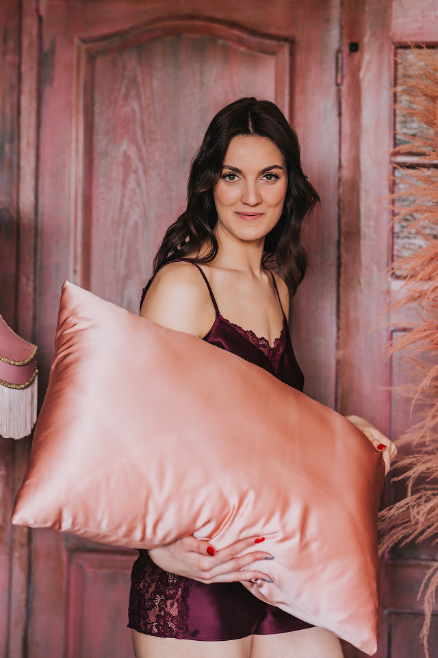 sieviete tur rokās spilvenu ar zīda spilvendrānu, rozā krāsa