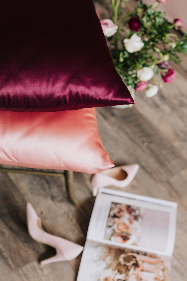 divi spilveni uz krēsla ar zīda spilvendrānām, rozā un bordo krāsā, skats uz spilvenu stūriem