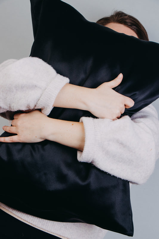 Black silk pillowcase, hands around and holding black pillow