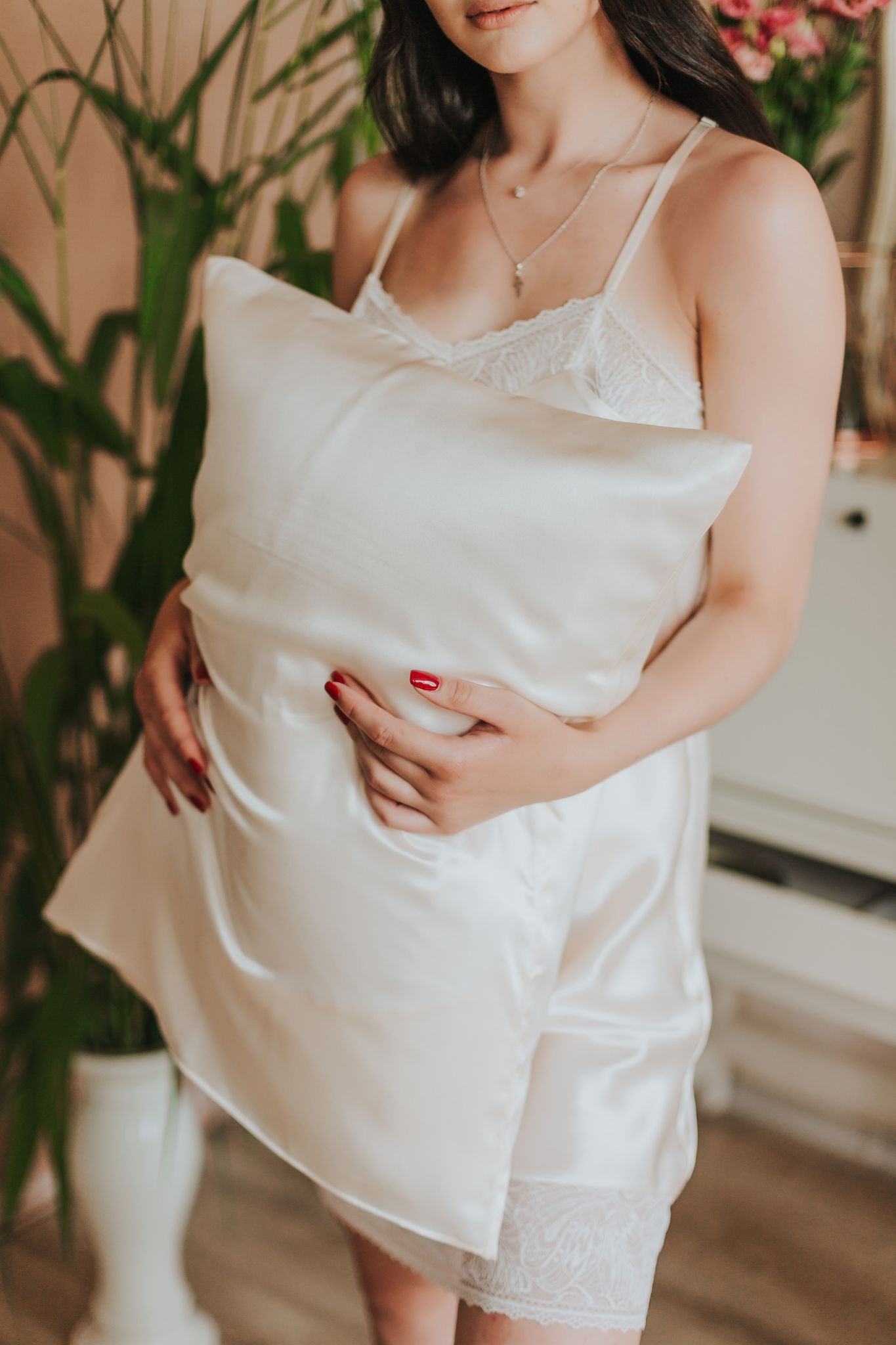 spilvens ar šampanieša krāsas zīda spilvendrānu sievietei rokās, skats no priekšpuses