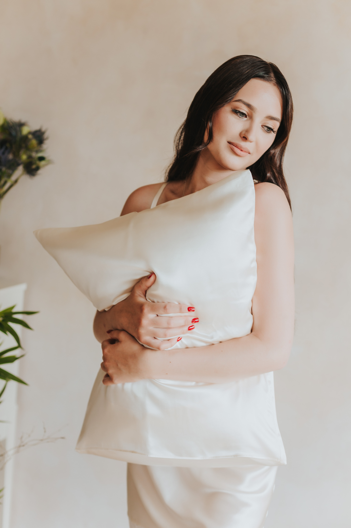 spilvens ar šampanieša krāsas zīda spilvendrānu sievietei rokās, skats no priekšpuses