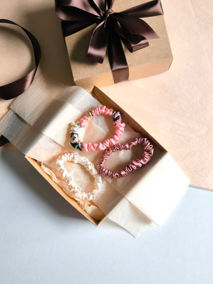 Pink hair ties in an open gift box with a brown ribbon on a light gray background