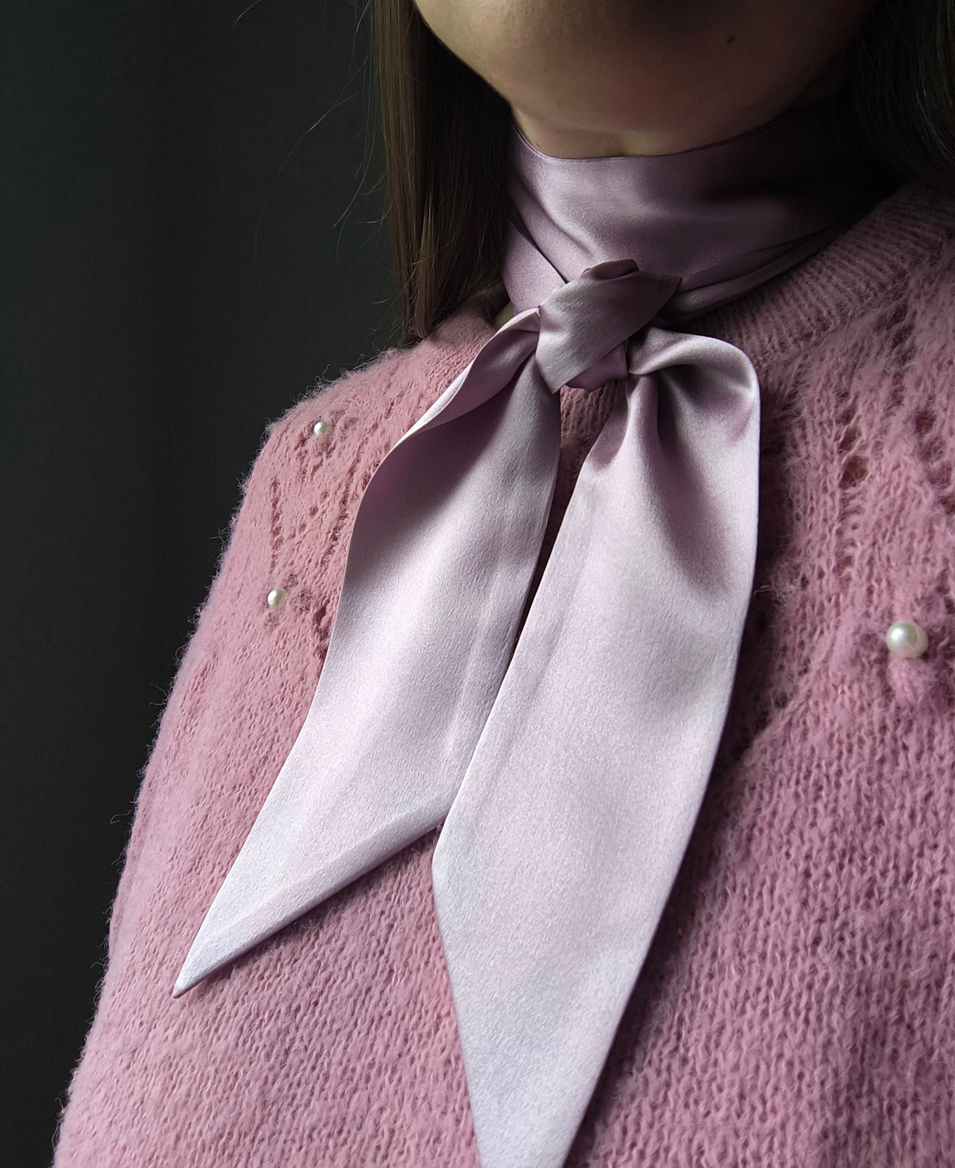 Person wearing a light pink knitted sweater with a matching scarf against a dark background