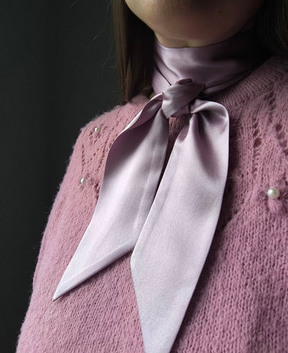 Person wearing a light pink knitted sweater with a matching scarf against a dark background