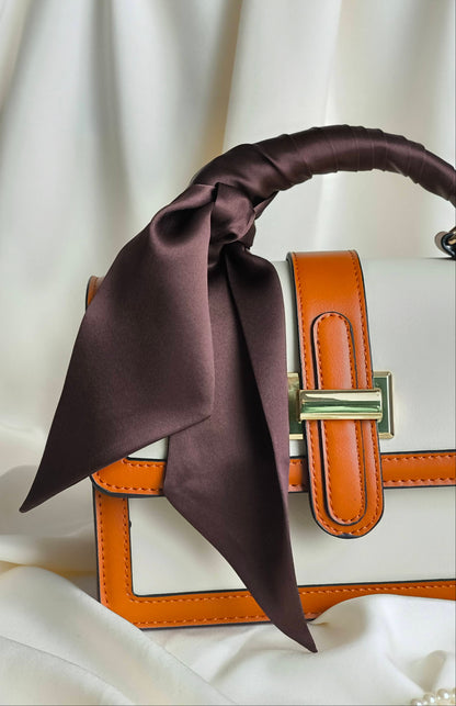 Brown satin scarf draped over a brown handbag on a white background