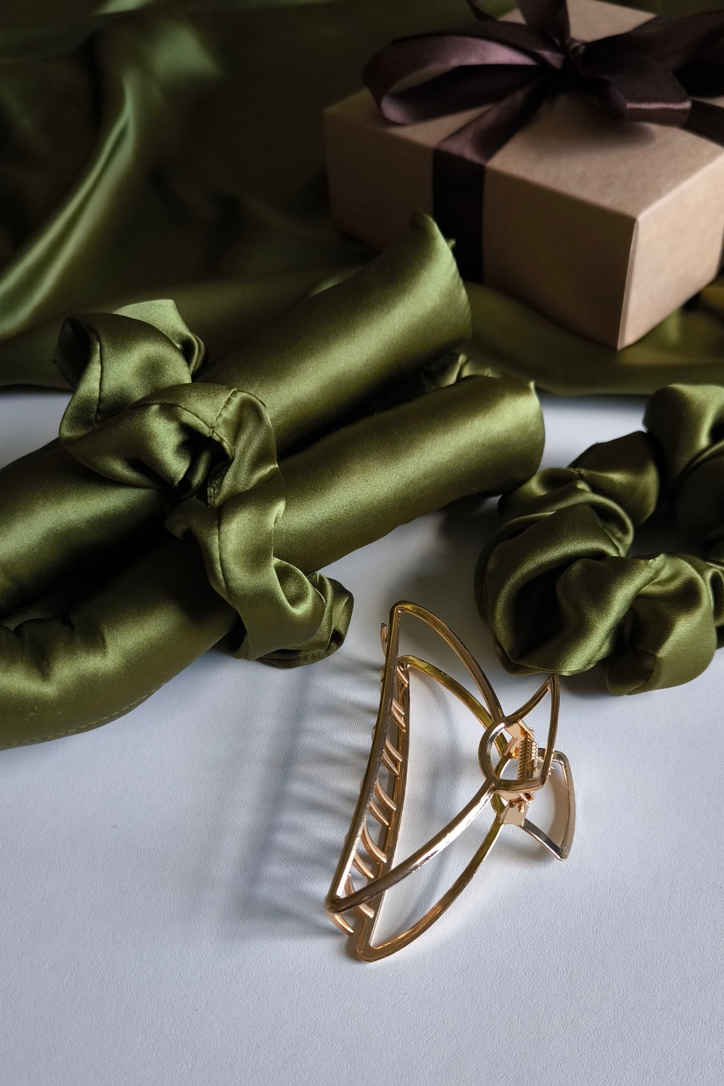 Gold hair clip on a white surface with green satin fabric and a brown gift box in the background.