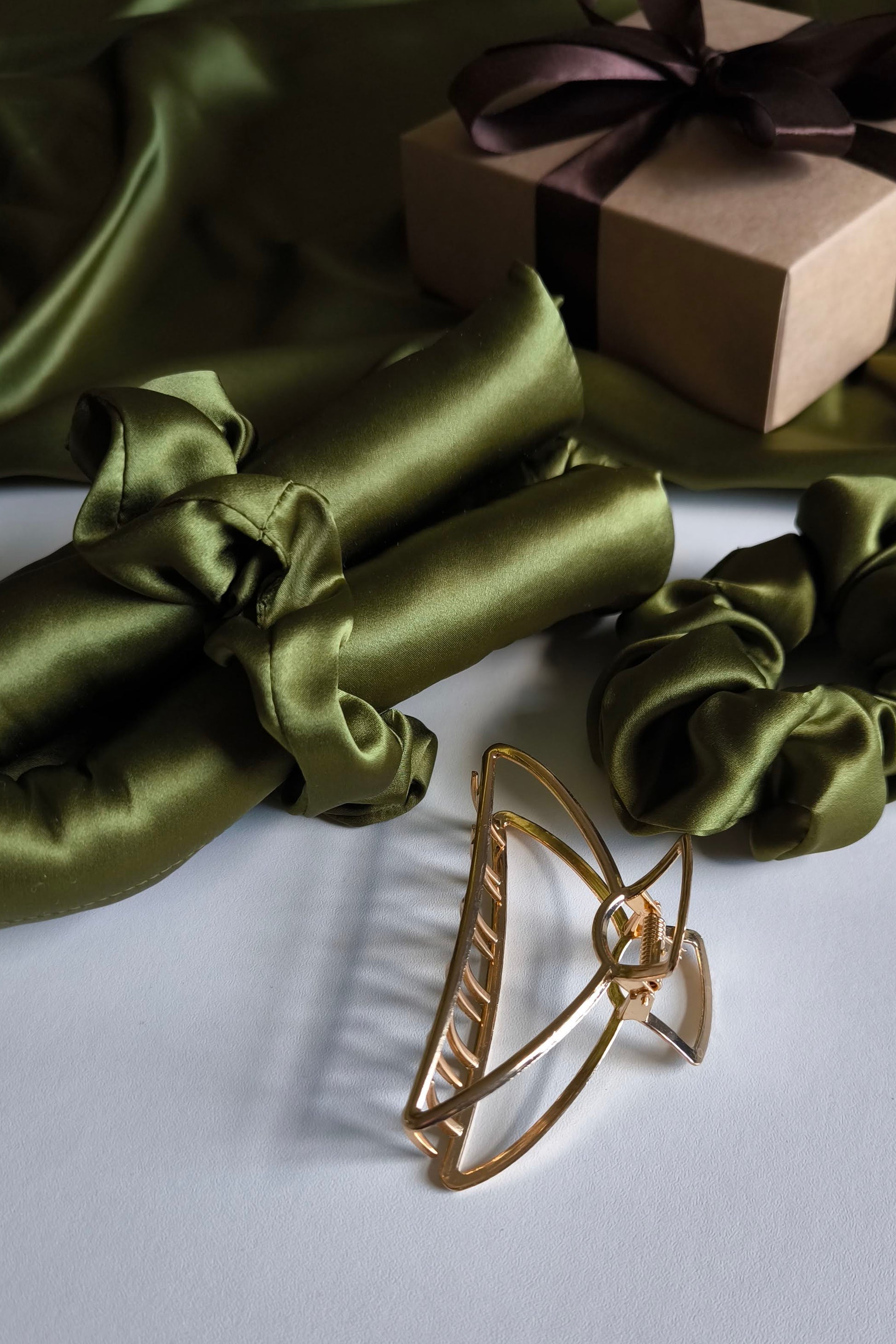 Gold hair clip on a white surface with green satin fabric and a brown gift box in the background.