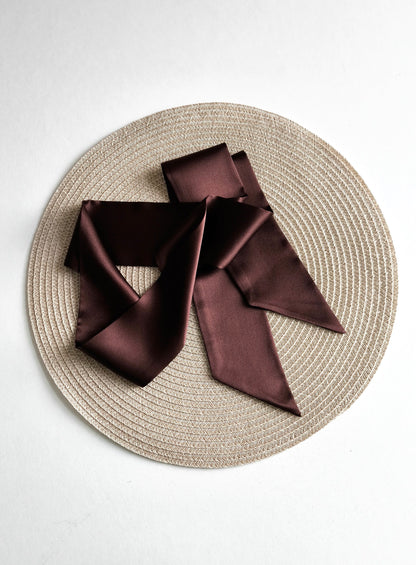 Brown satin scarf on a textured beige plate with a white background