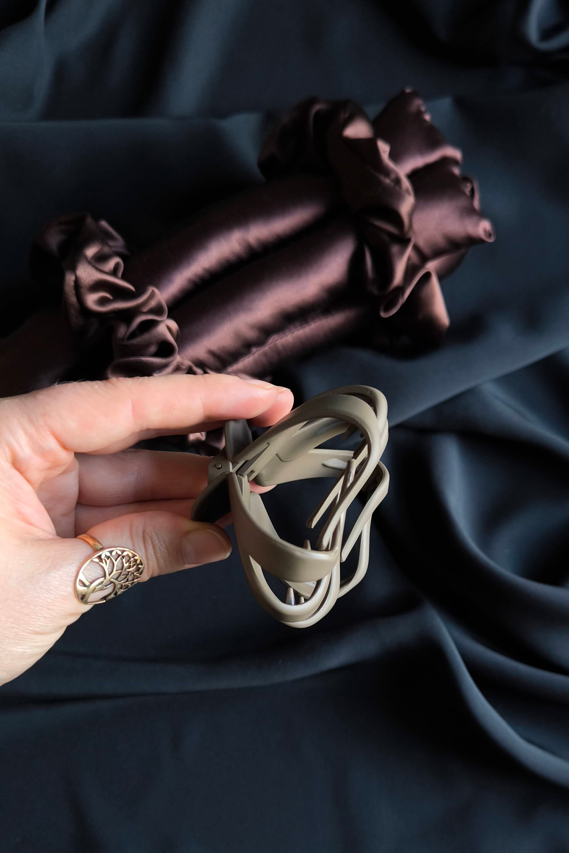 Hand holding a small hair clip against a dark fabric background