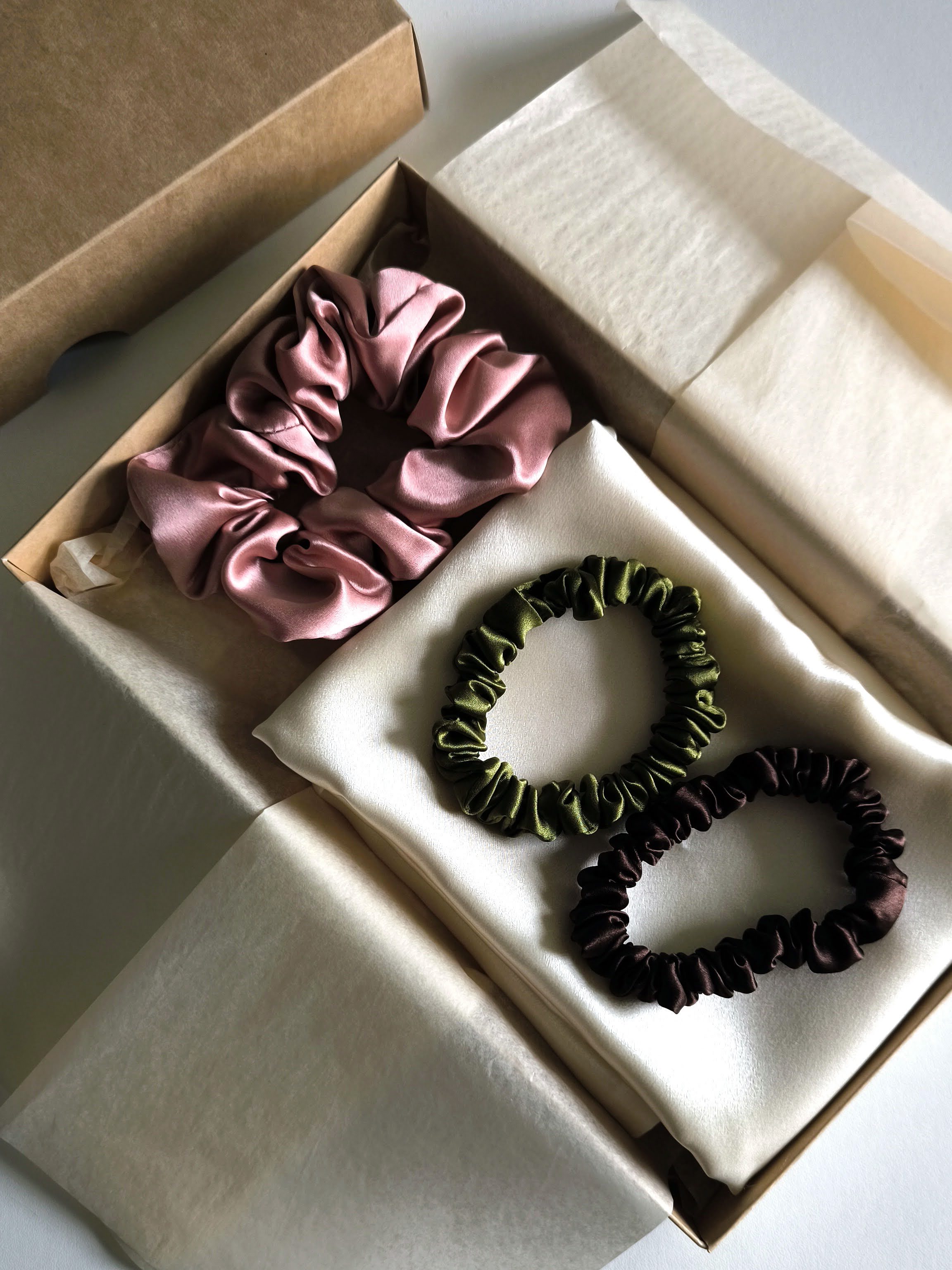 Two scrunchies, one pink and one brown, in an open box on a white surface.