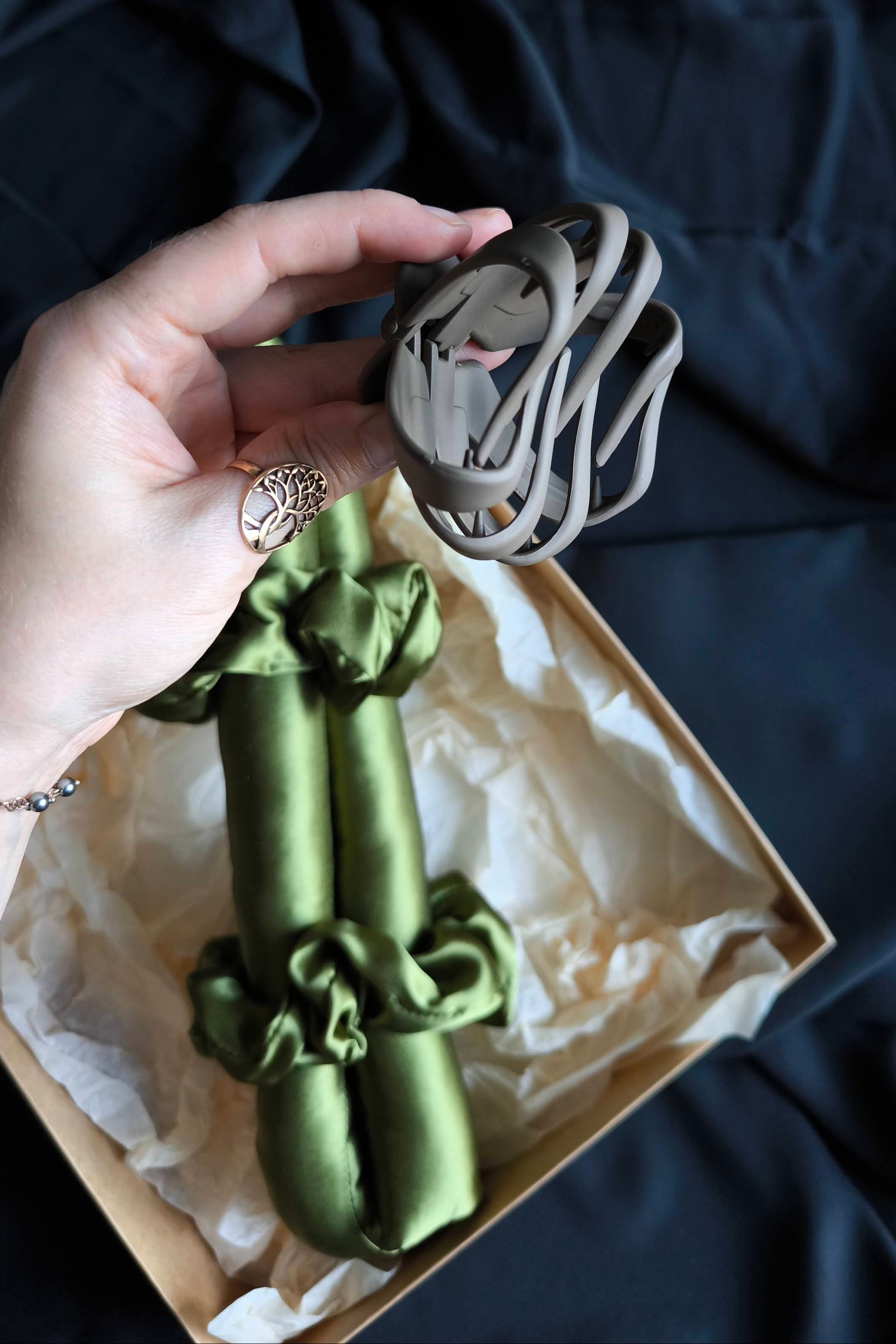 Green satin hair curler with decorative bow held over a box on a dark fabric background