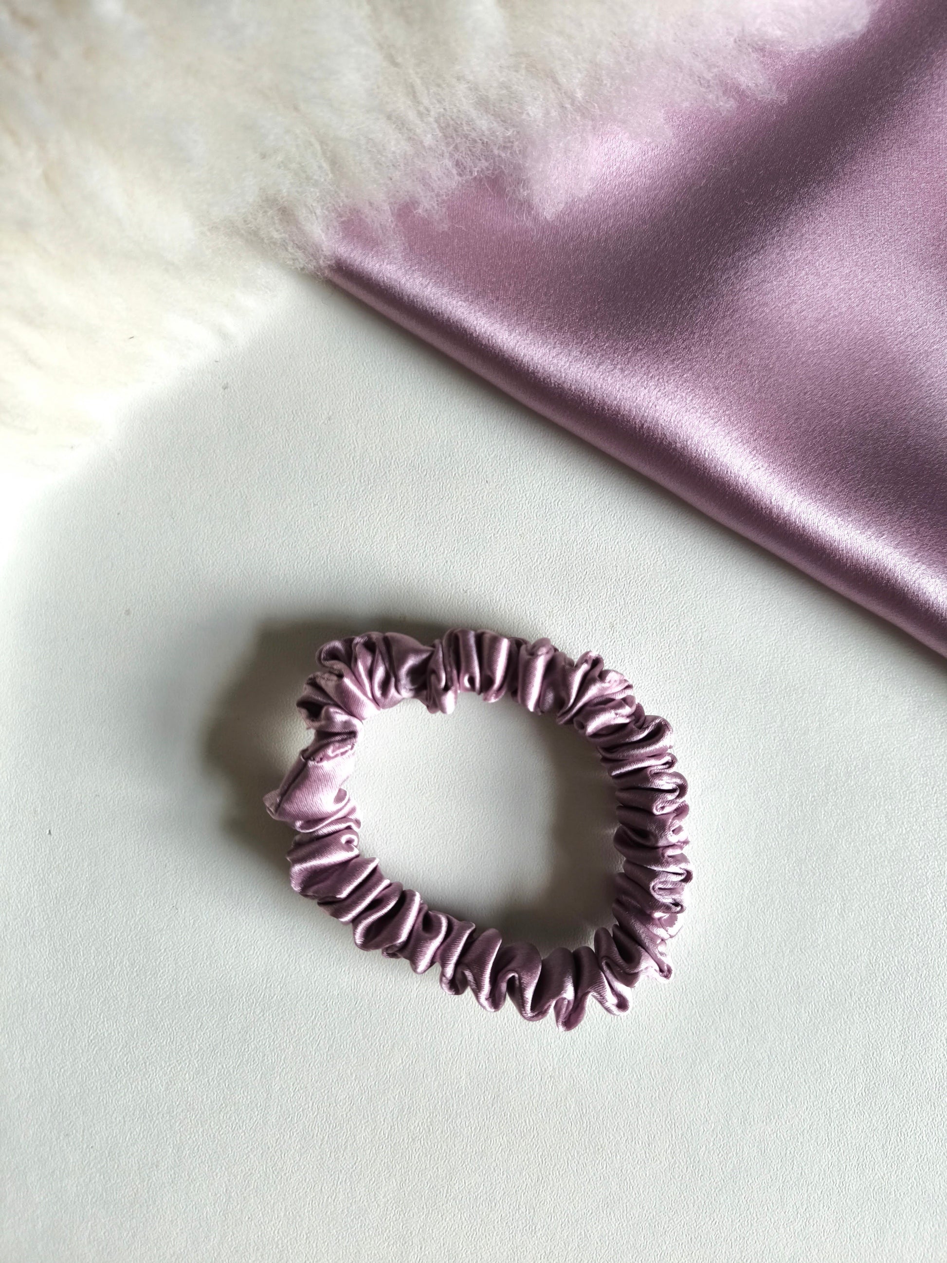 Purple scrunchie on a light surface with a soft pink fabric background