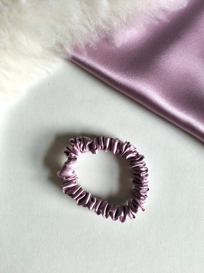 Purple scrunchie on a light surface with a soft pink fabric background