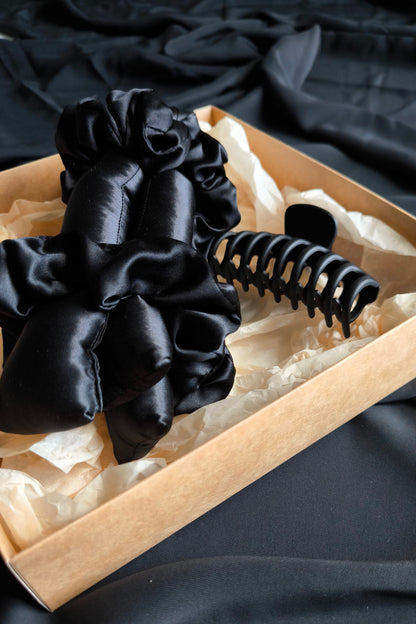 Black satin hair scrunchies and a black heatless curler in a box on a dark fabric background