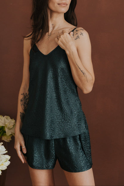 Woman wearing a dark green slip and shorts set against a brown background