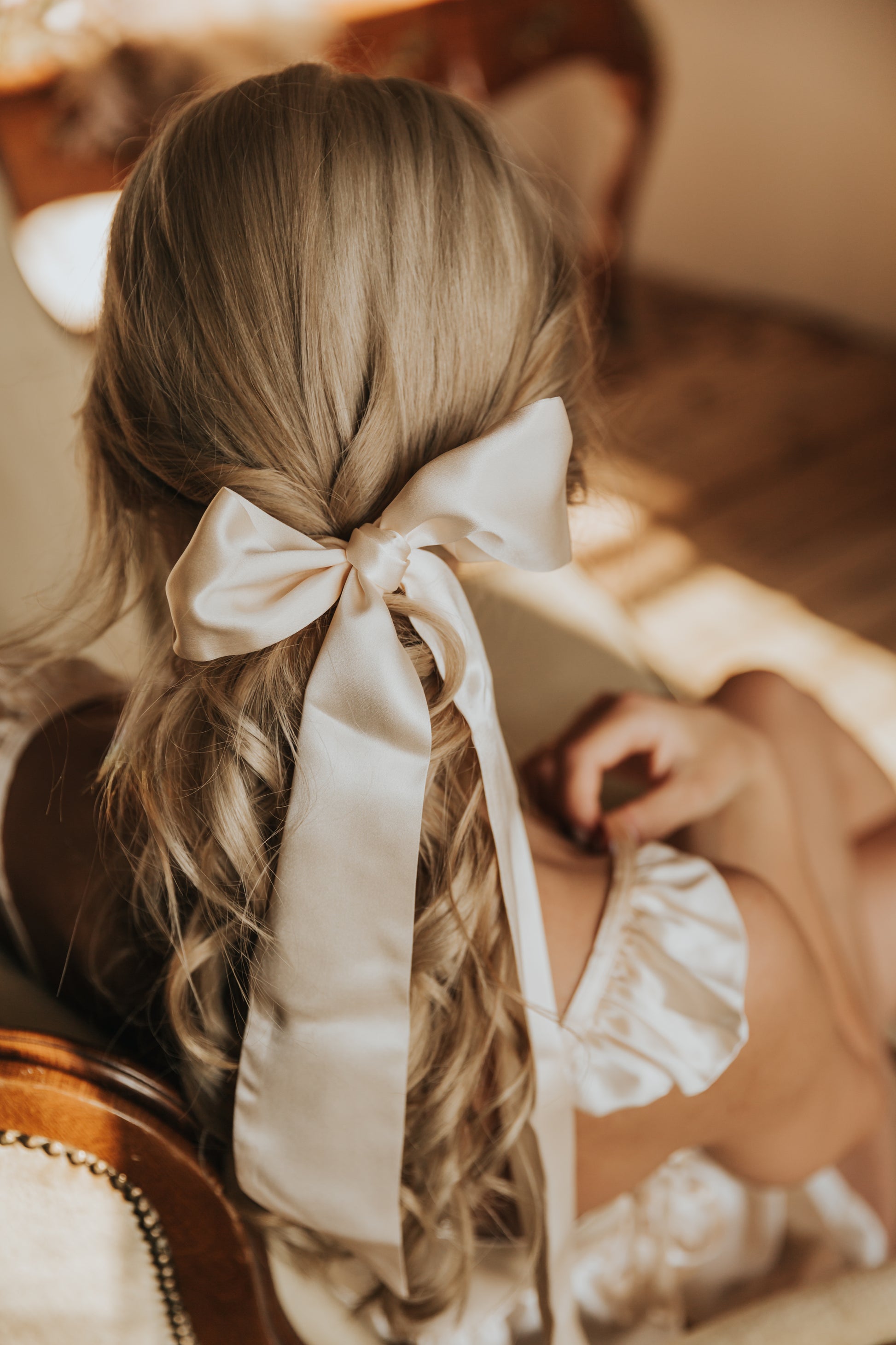A woman with her hair styled and adorned with a champagne color silk ribbon bow.
