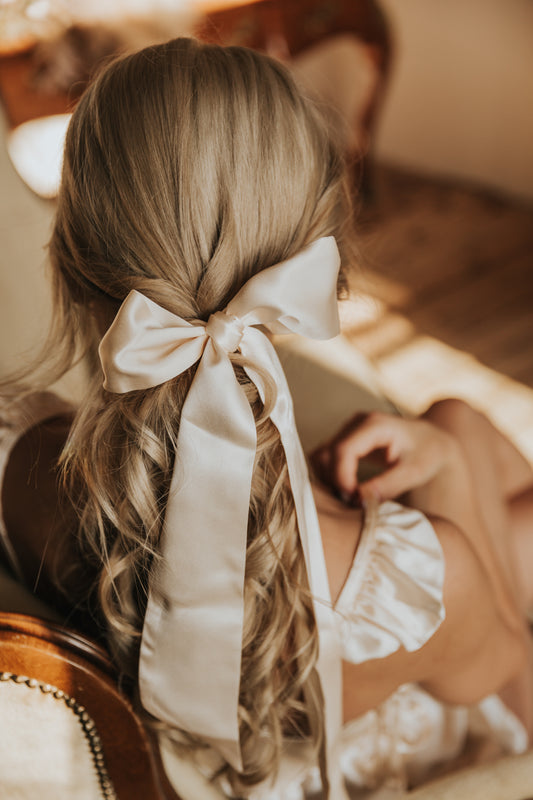 A woman with her hair styled and adorned with a champagne color silk ribbon bow.