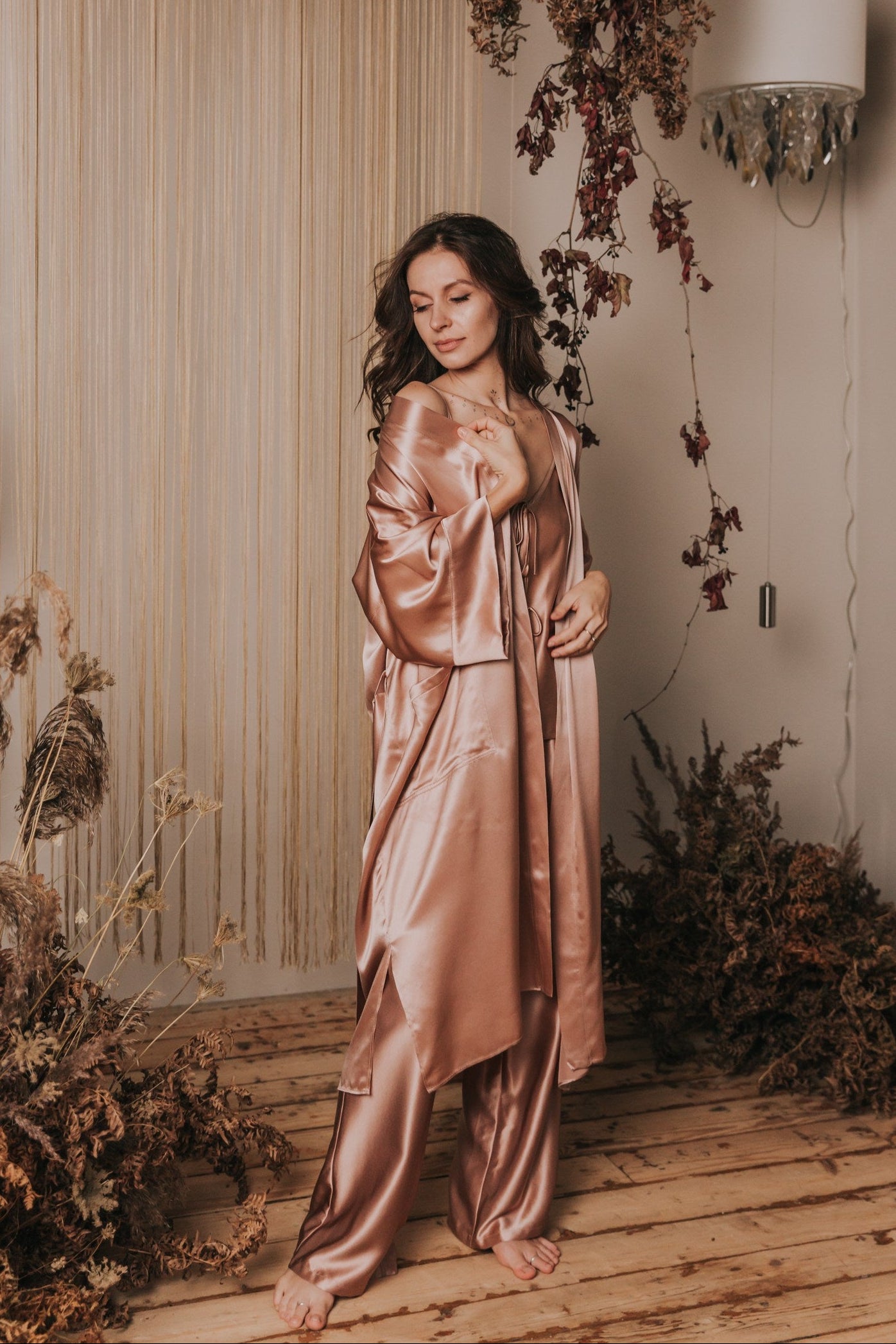 Woman in a pink satin dress standing in a decorated indoor setting with flowers and lights.