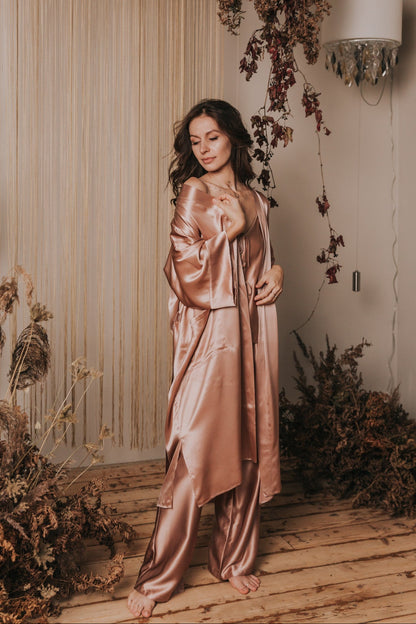 Woman in a pink satin dress standing in a decorated indoor setting with flowers and lights.