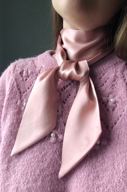 Person wearing a pink scarf tied around their neck against a dark background