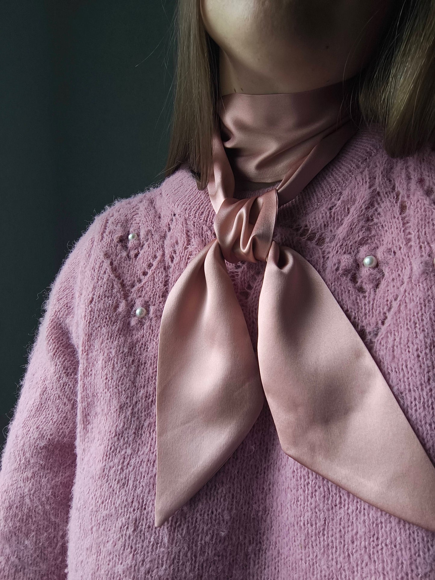 Person wearing a pink knitted sweater with a matching pink silk scarf
