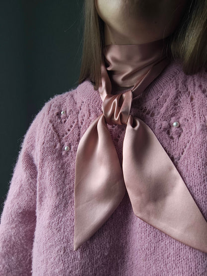Person wearing a pink knitted sweater with a matching pink silk scarf