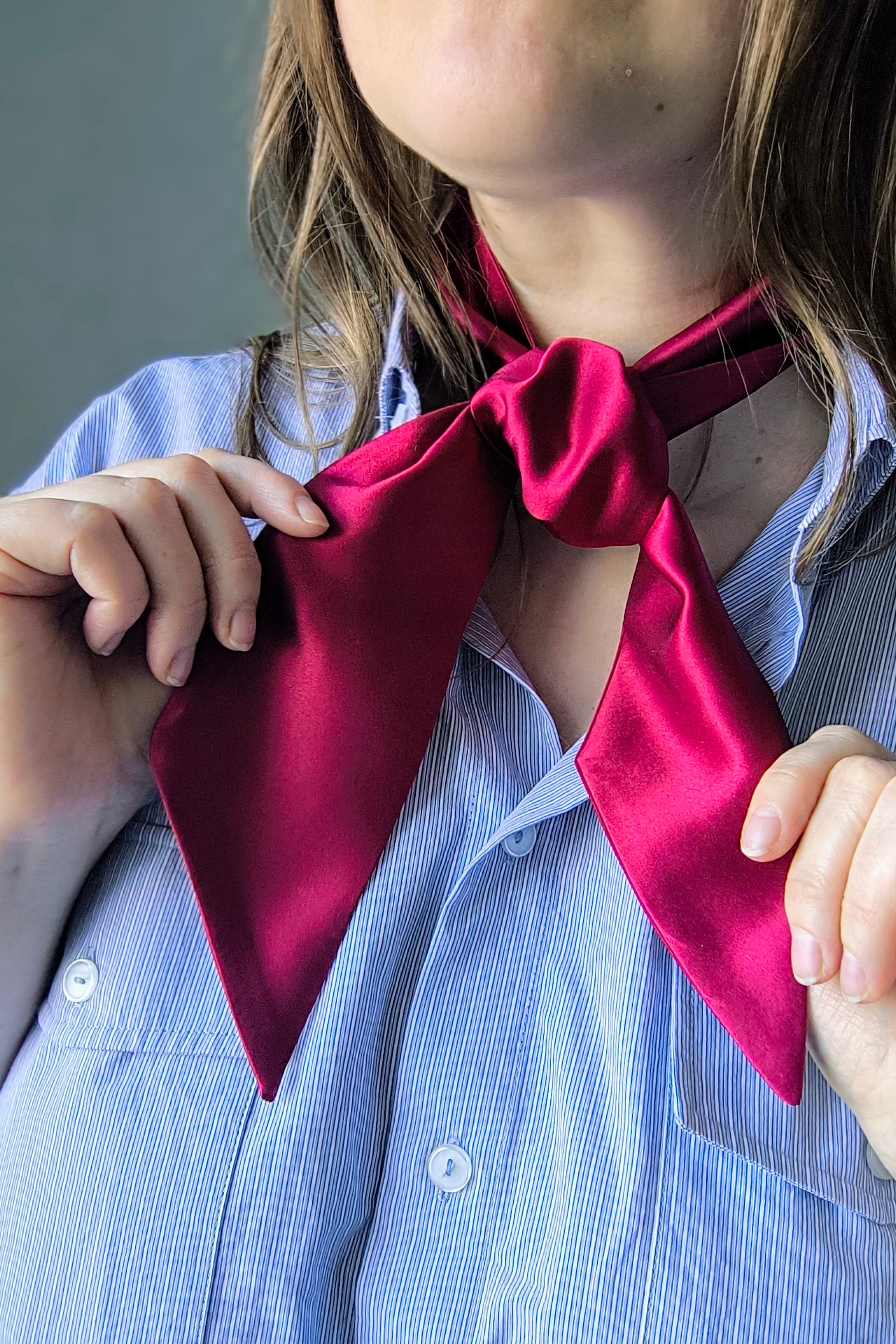 A person wearing a wine red silk ribbon around their neck, with the ribbon flowing down to form a bow at the front.