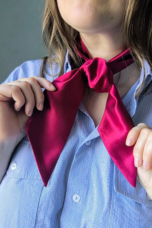 A person wearing a wine red silk ribbon around their neck, with the ribbon flowing down to form a bow at the front.