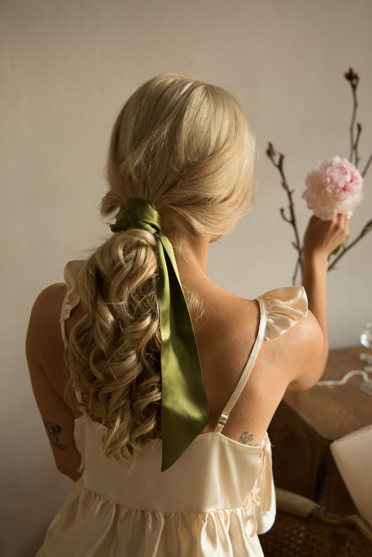 Woman with styled hair holding a pink flower in an indoor setting