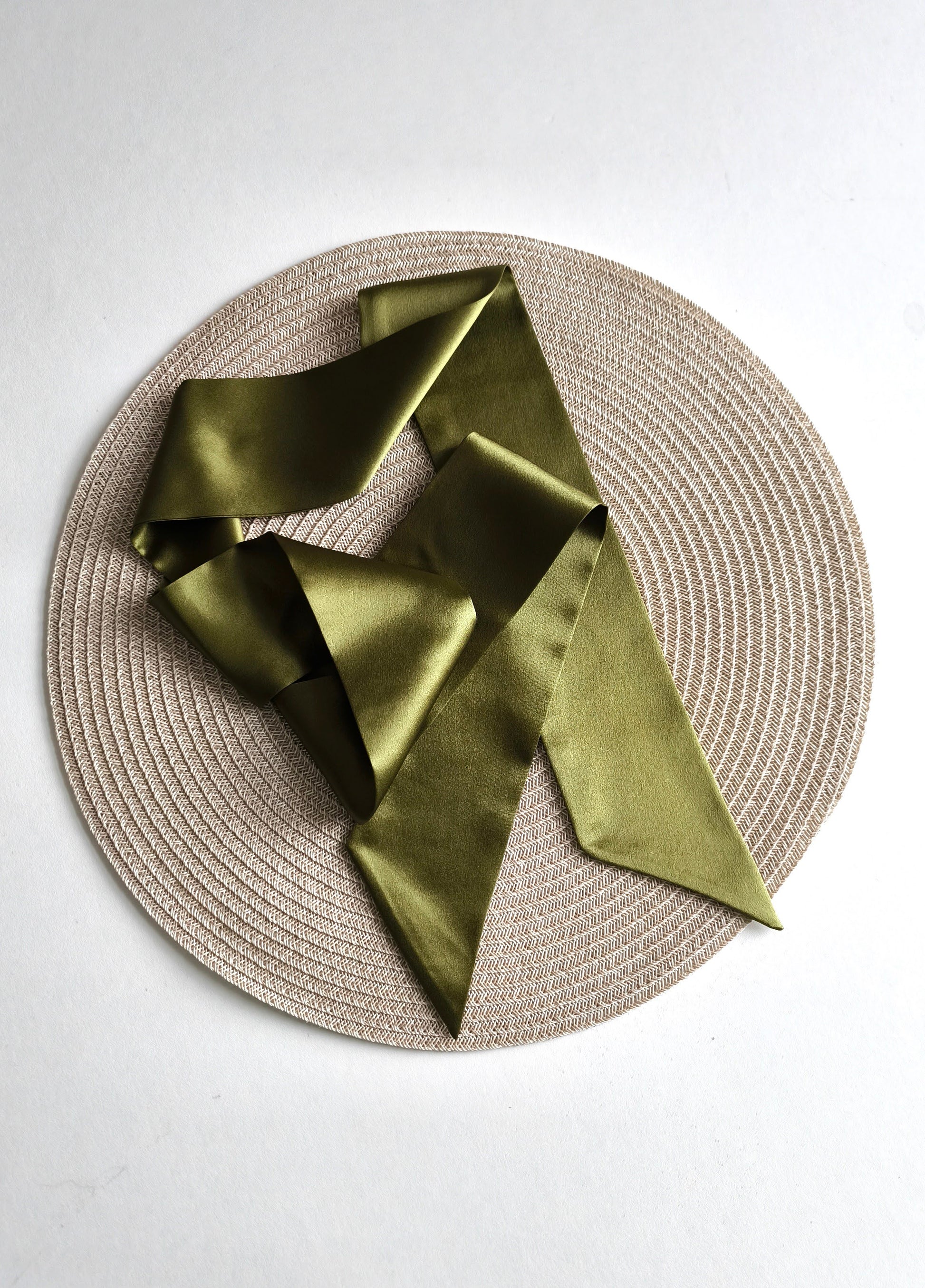 Green satin scarf on a round woven placemat with a white background