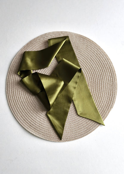 Green satin scarf on a round woven placemat with a white background