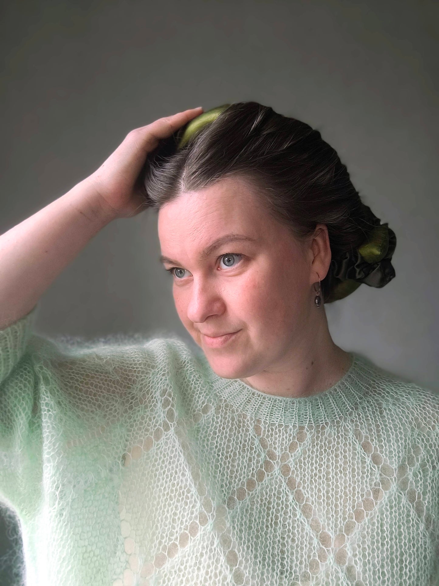 Woman with a bun and green sweater against a gray background