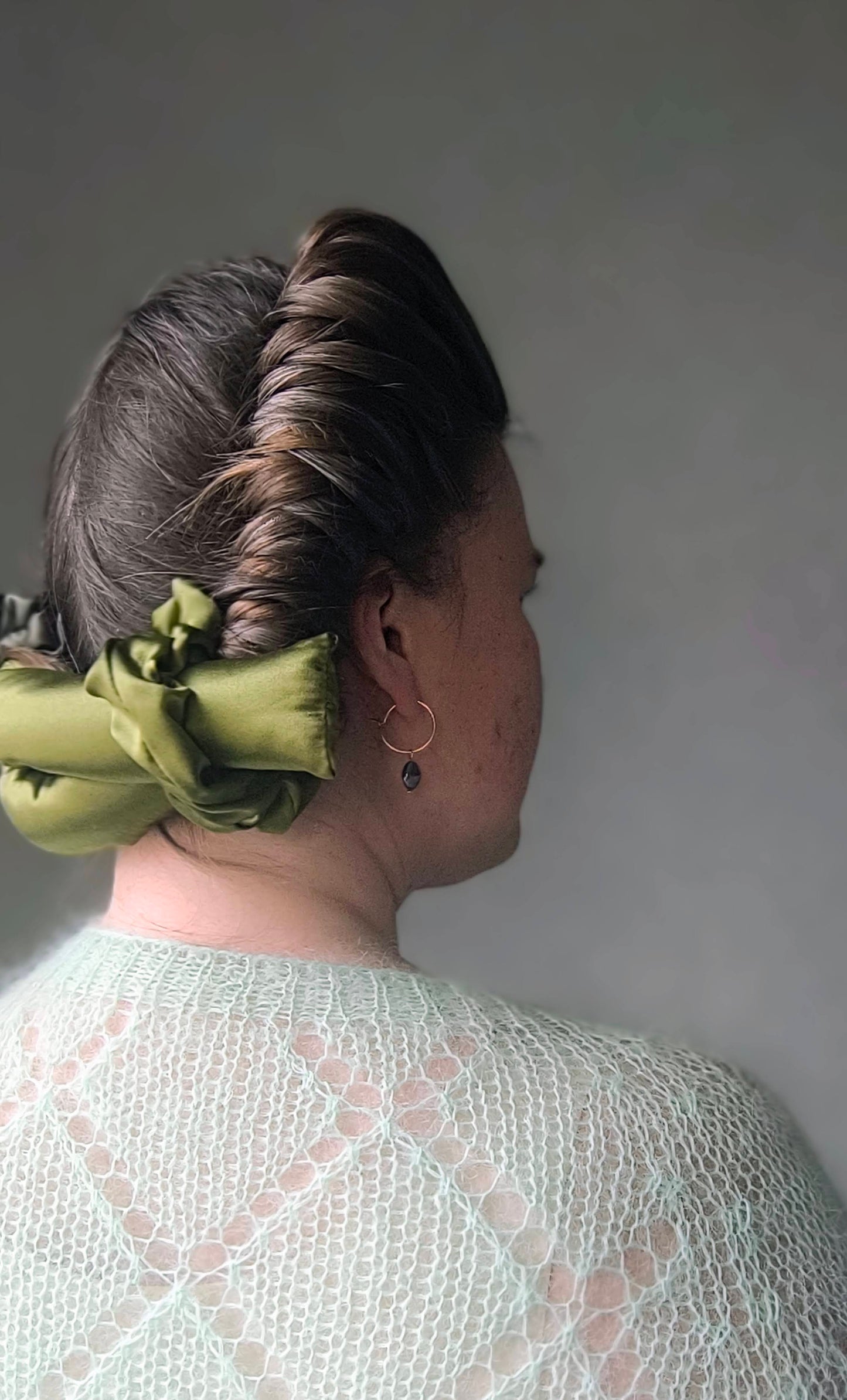 Person with silk hair curlers and green scrunchie against a gray background