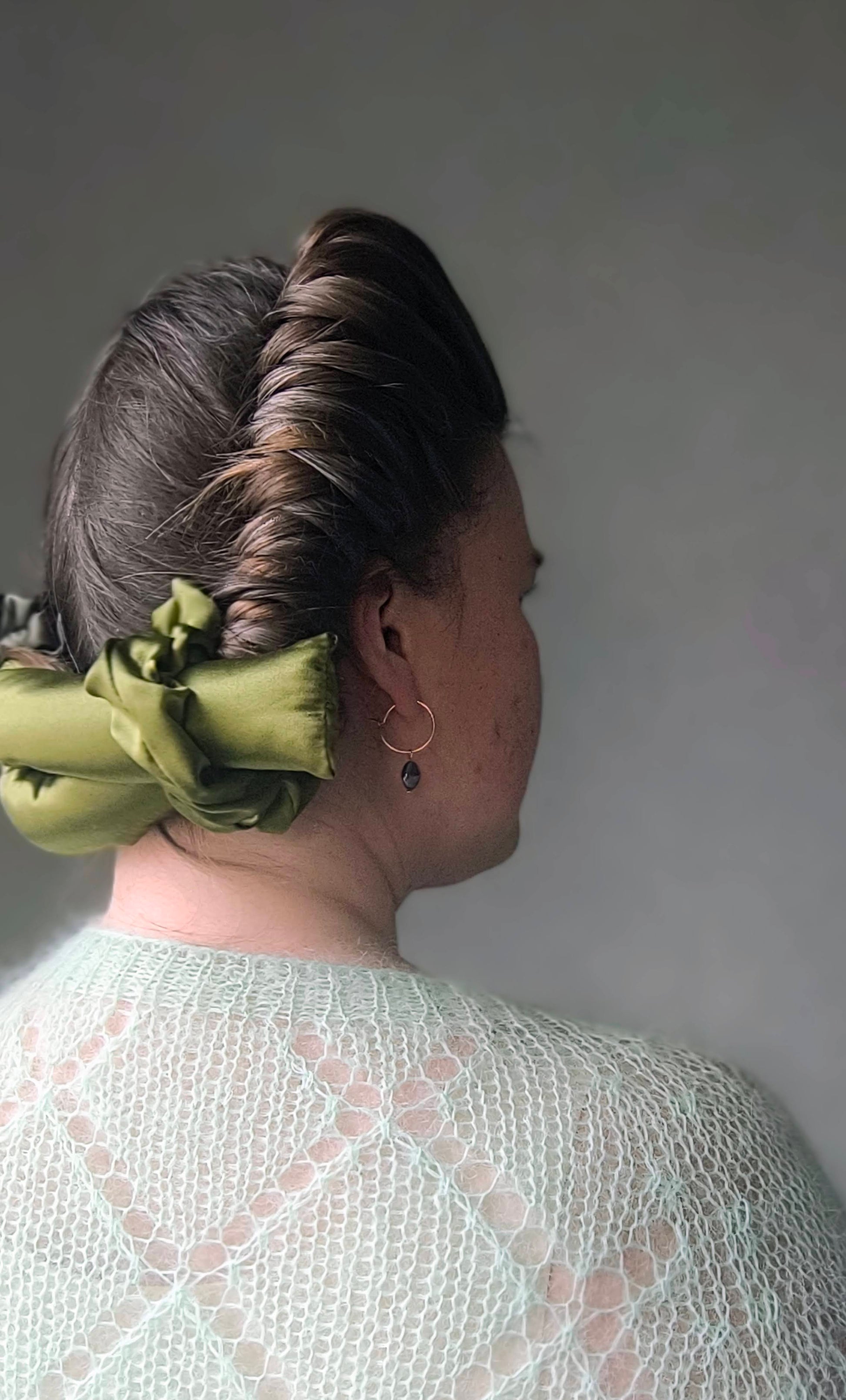 Person with silk hair curlers and green scrunchie against a gray background