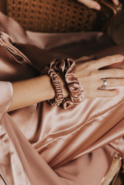 Person wearing a pink silk outfit with silk scrunchies sitting on a dark background.