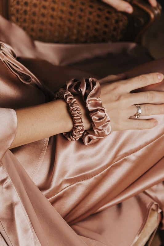 Person wearing a pink silk outfit with silk scrunchies sitting on a dark background.