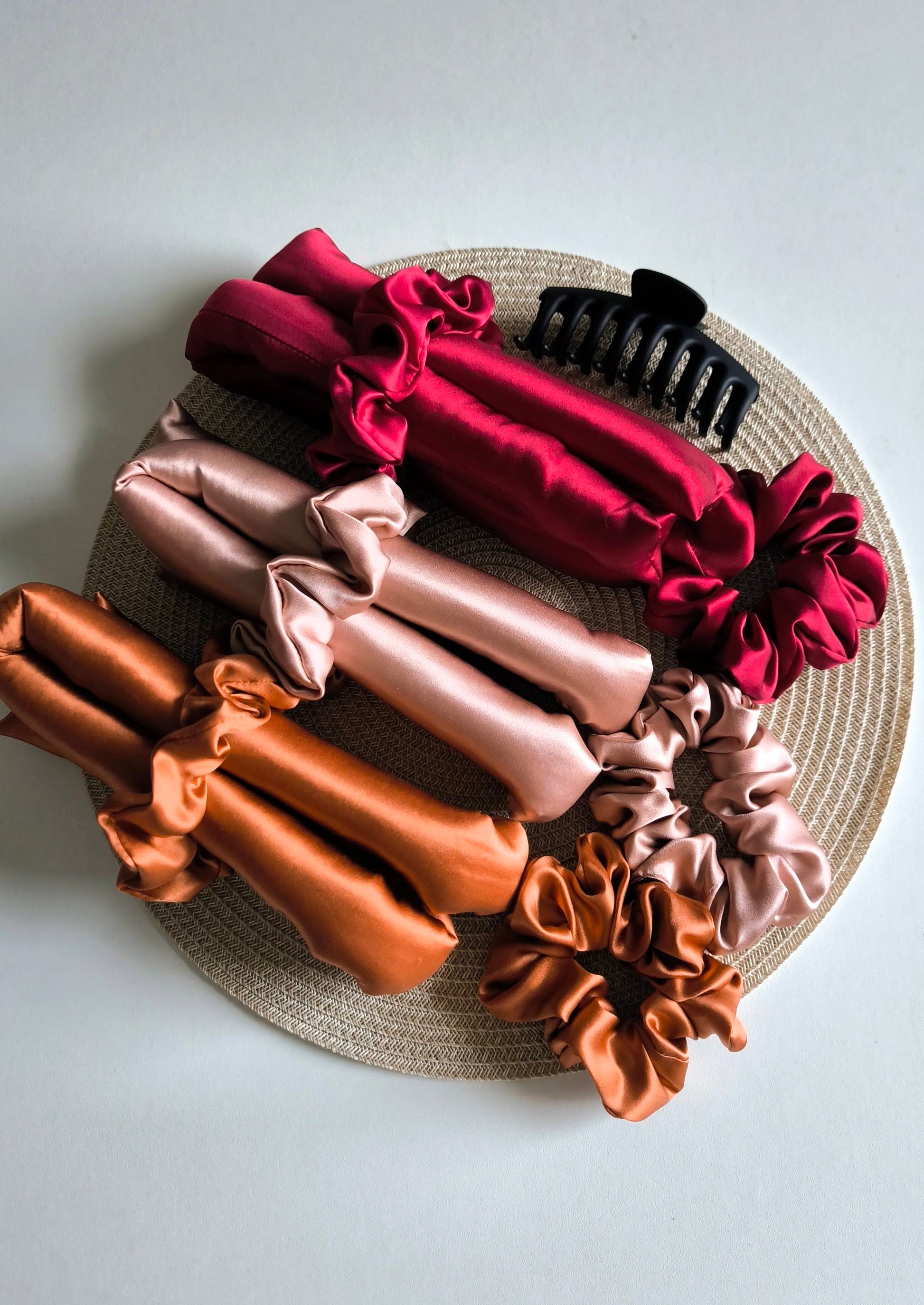 Set of colorful silk hair scrunchies and curlers on a woven mat