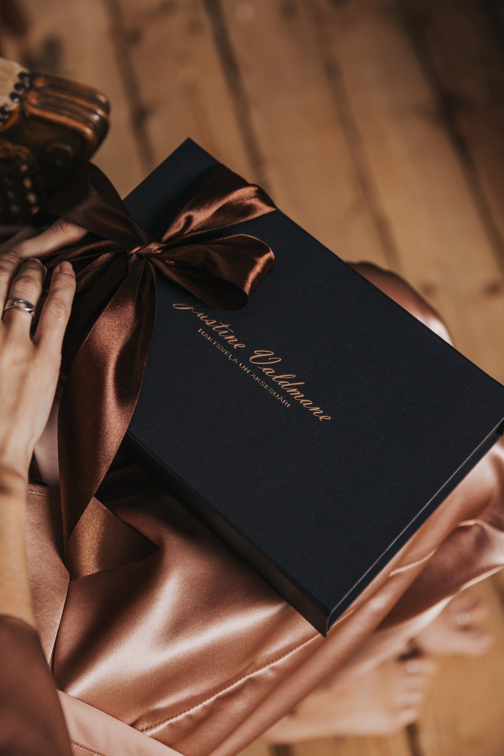 Black gift box with a brown ribbon held by hands on a wooden surface