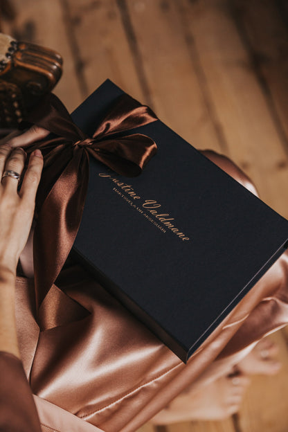 Black gift box with a brown ribbon held by hands on a wooden surface