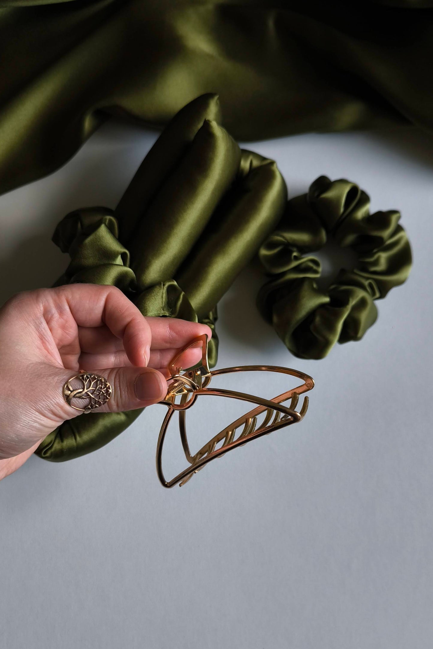 Green satin scrunchies on a white surface with a hand holding a hair clip.