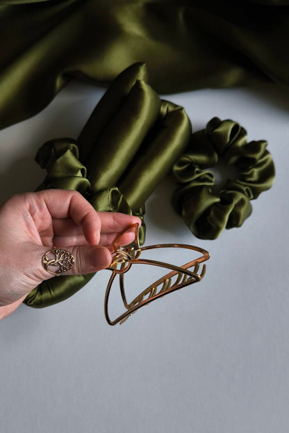 Green satin scrunchies on a white surface with a hand holding a hair clip.