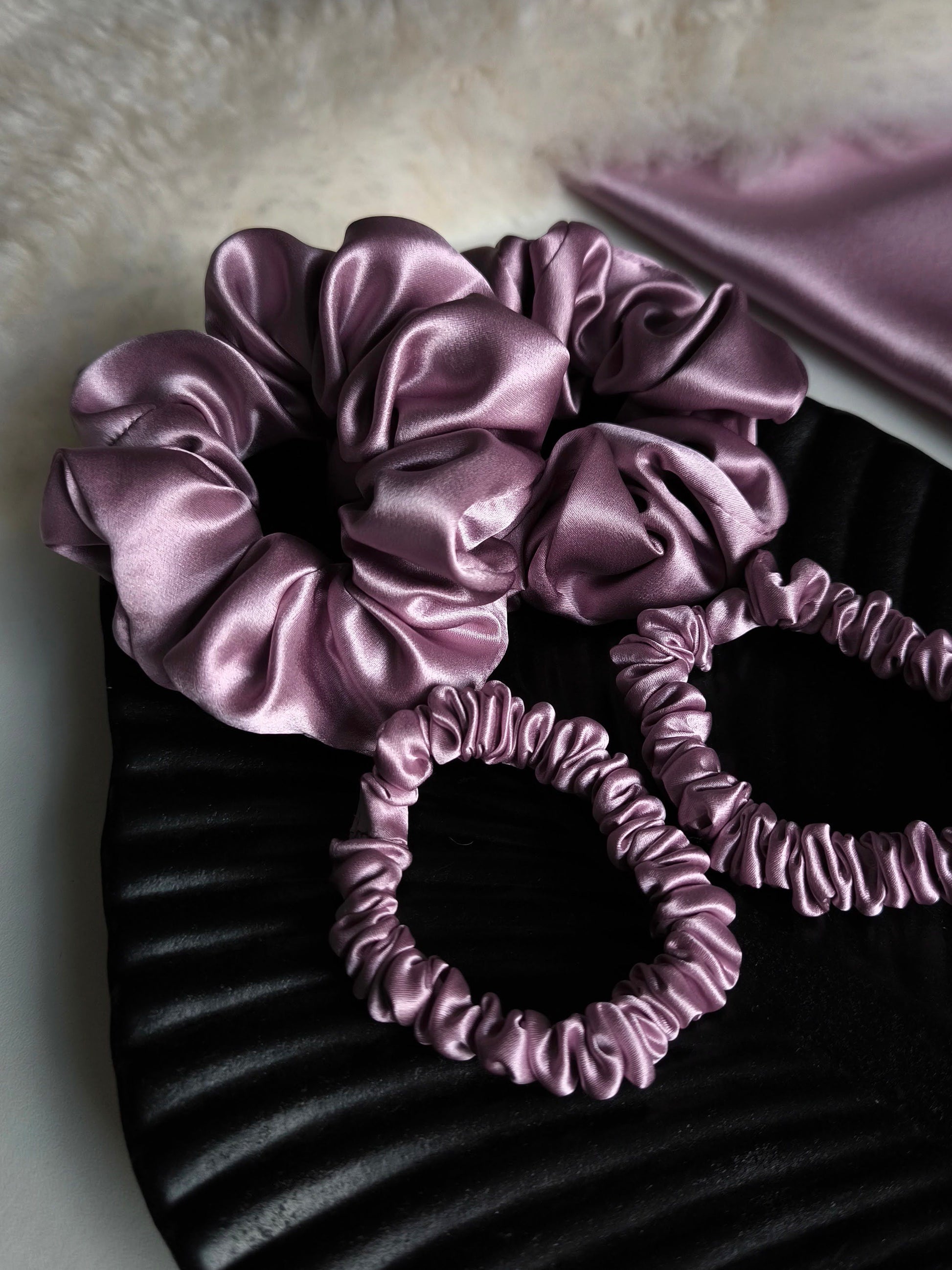 Set of purple satin hair scrunchies on a textured surface