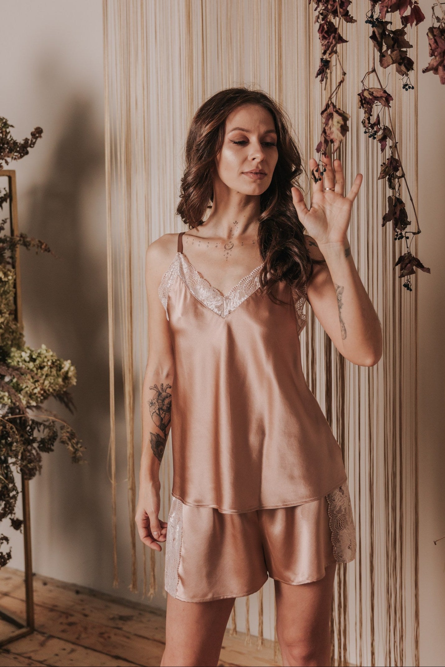 Woman wearing a pink satin nightgown in a softly lit room with floral decorations.