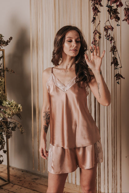 Woman wearing a pink satin nightgown in a softly lit room with floral decorations.