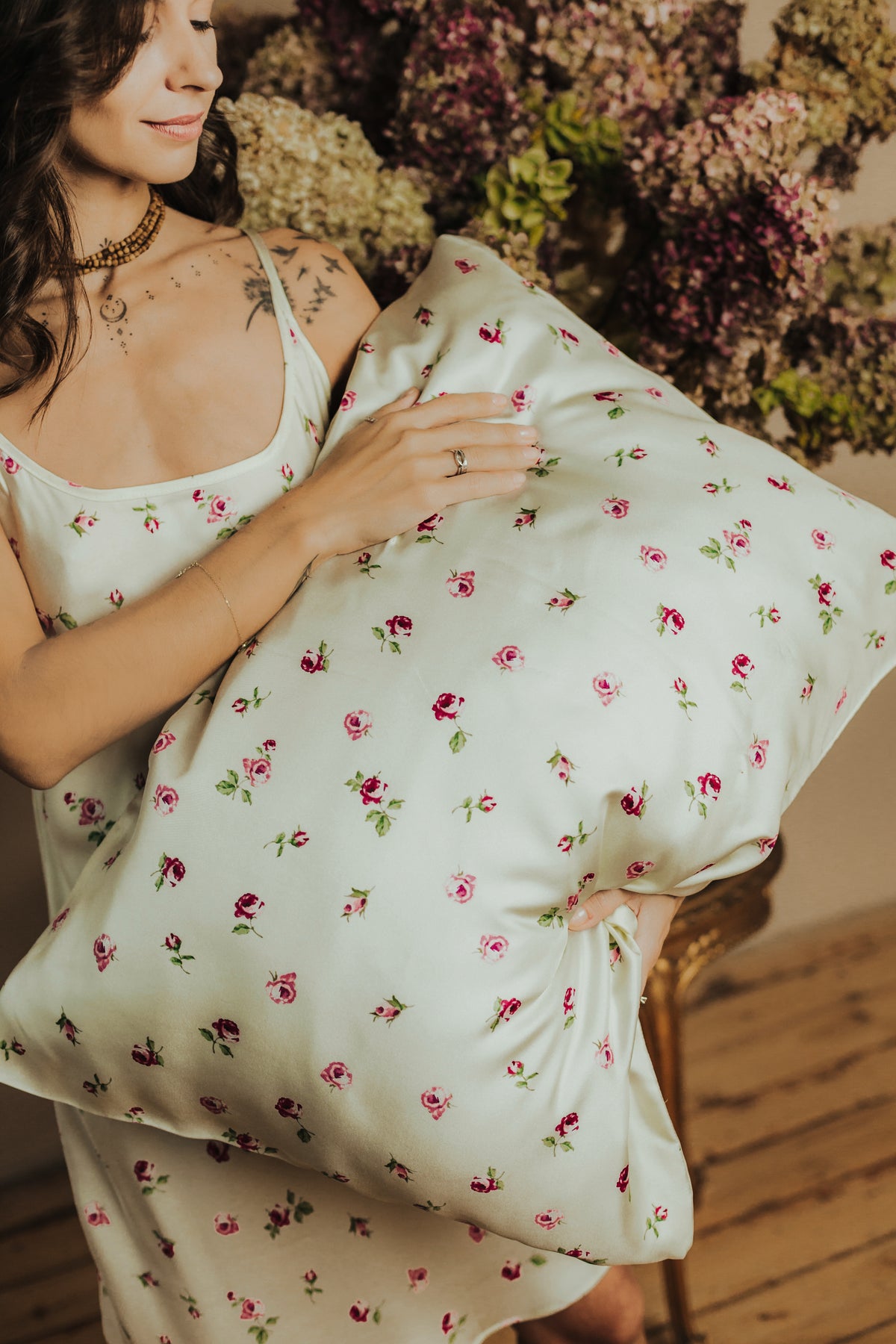 A woman in a matching white twill slip dress holds a large butter-yellow color pillow with a pink and green floral print.